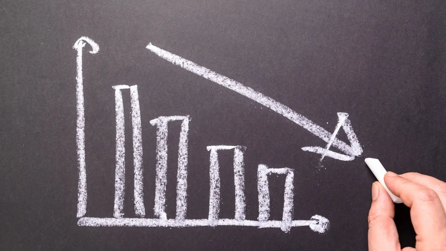 Chalk drawing of declining bar chart with downward arrow on blackboard.