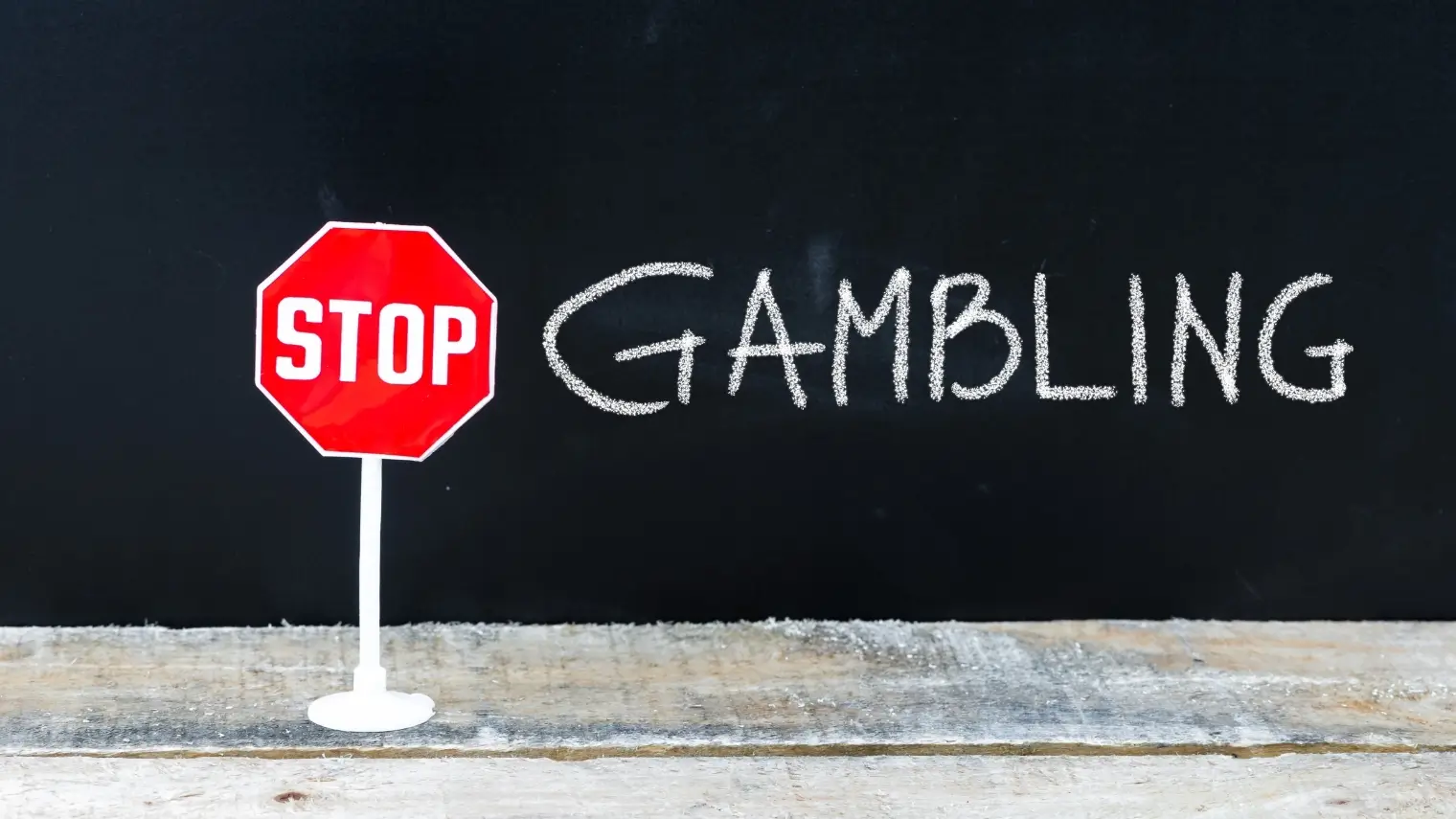 Stop sign next to the words “Stop Gambling” written in chalk on blackboard.