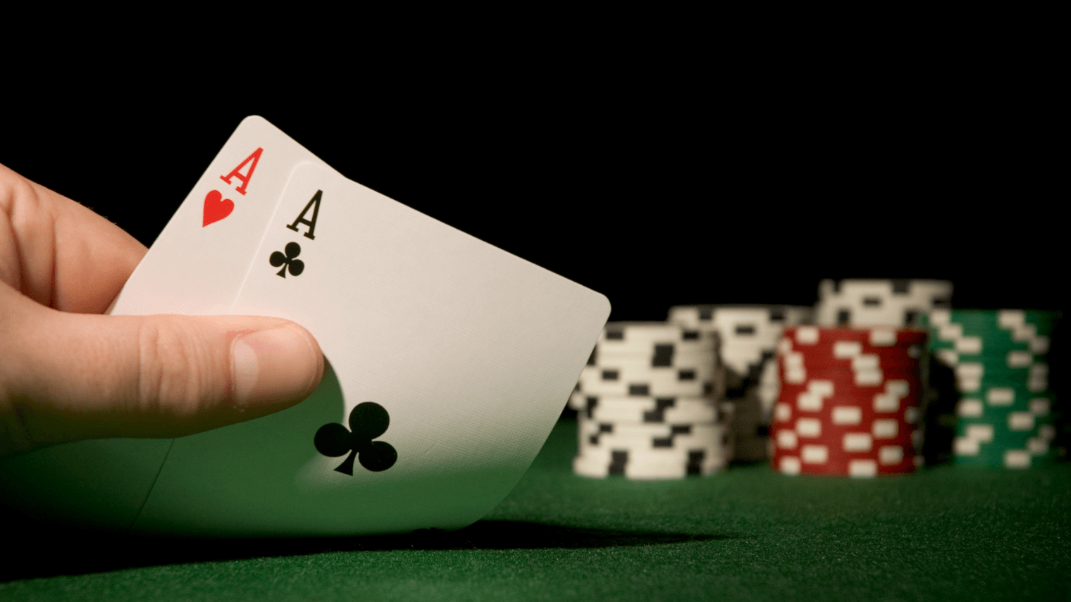 Pocket aces held at a poker table with stacks of chips in the background, illustrating opening poker hands for 6-max cash games.