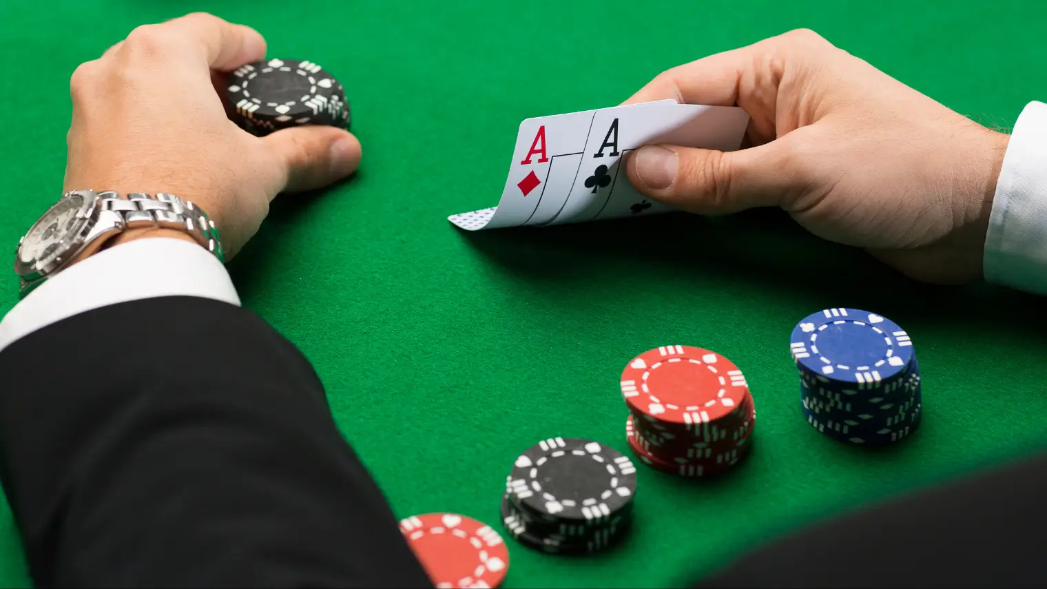 Poker player holding pocket aces with stacks of poker chips on a green felt table.