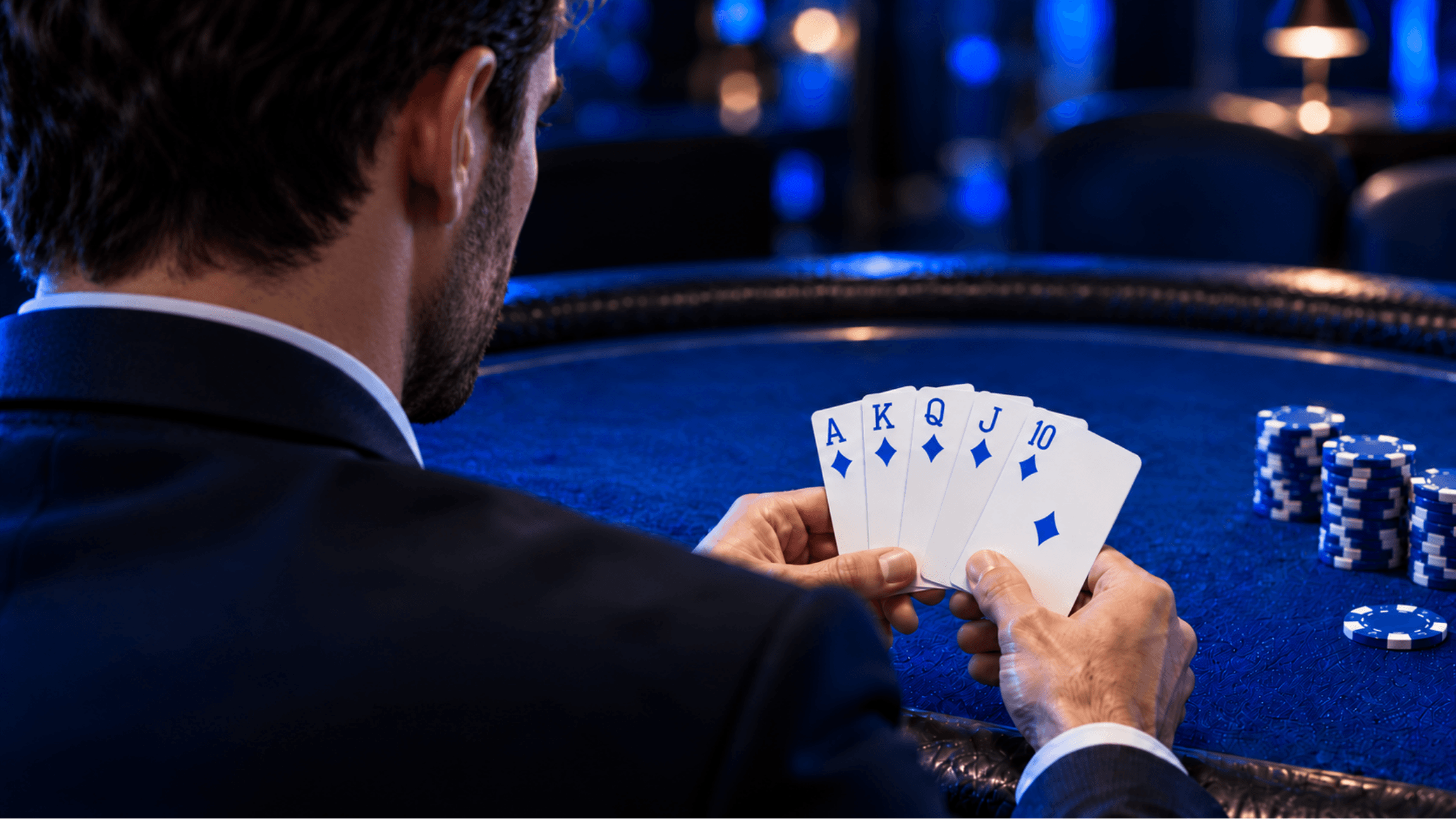 Poker player holding a royal flush in blue diamonds at a poker table.